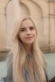 A woman with long blonde hair standing in front of a fountain.