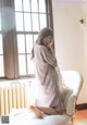 A woman sitting on a white chair in front of a window.