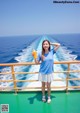 A woman standing on the deck of a boat holding a bottle of orange juice.