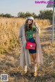 A woman standing in a field with a red bag.