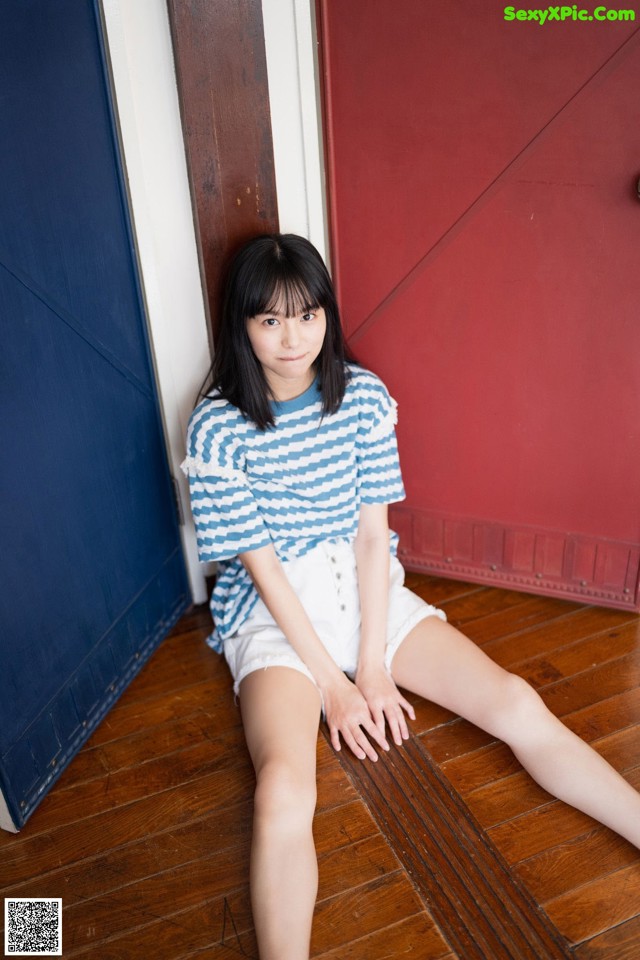 A woman sitting on the floor in front of a red door.