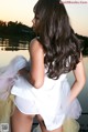 A woman in a white dress is posing by the water.