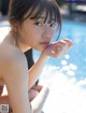 A woman in a bikini sitting by a swimming pool.