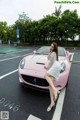 A woman sitting on the hood of a pink sports car.