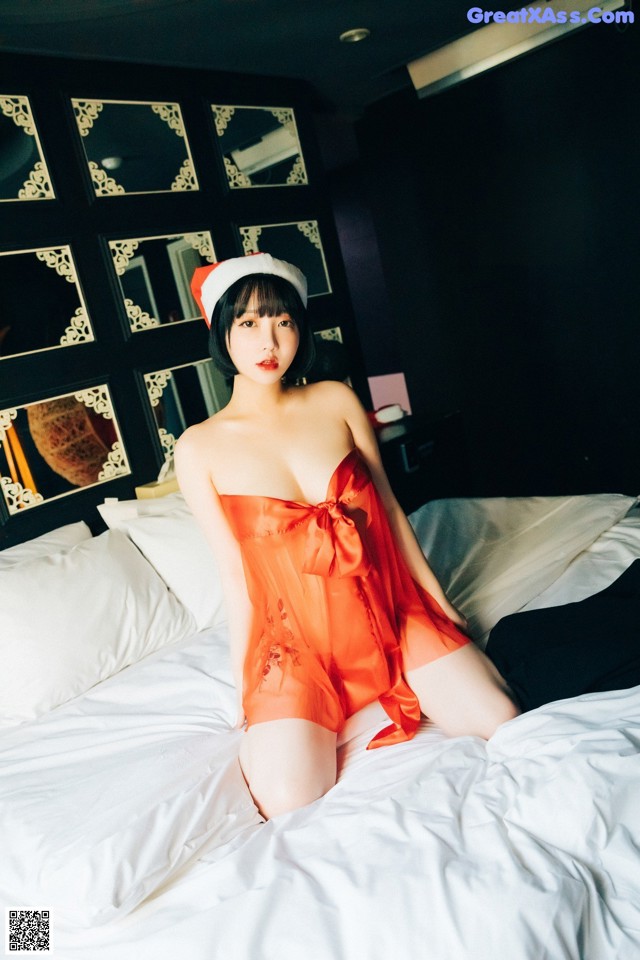 A woman in a red dress sitting on a bed.